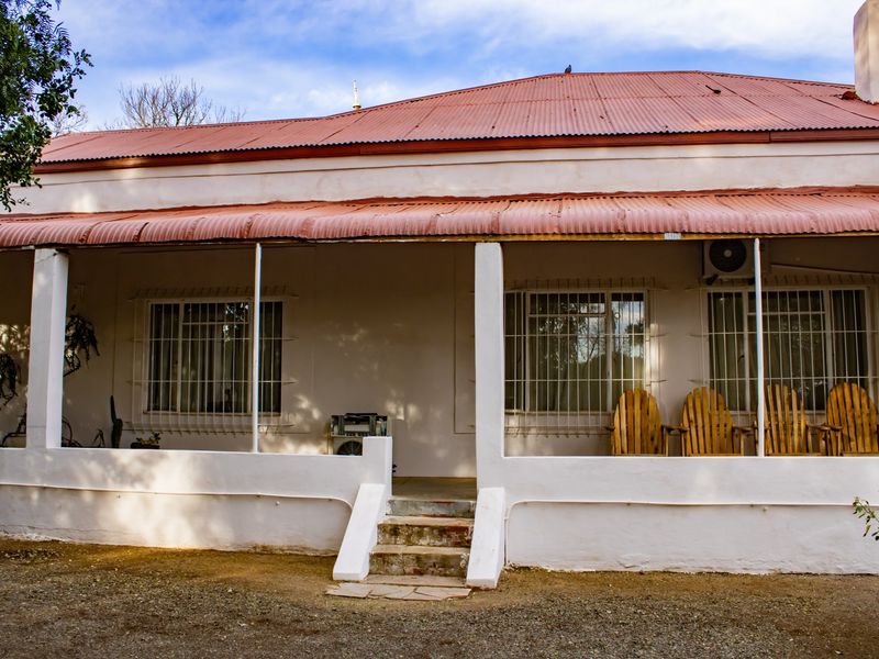 A rear view of the house featuring a covered veranda with a corrugated metal roof, security-barred windows, and an external air conditioning unit.
