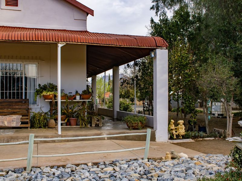 A covered patio area featuring concrete flooring, support pillars, and a corrugated metal roof with visible signs of weathering.