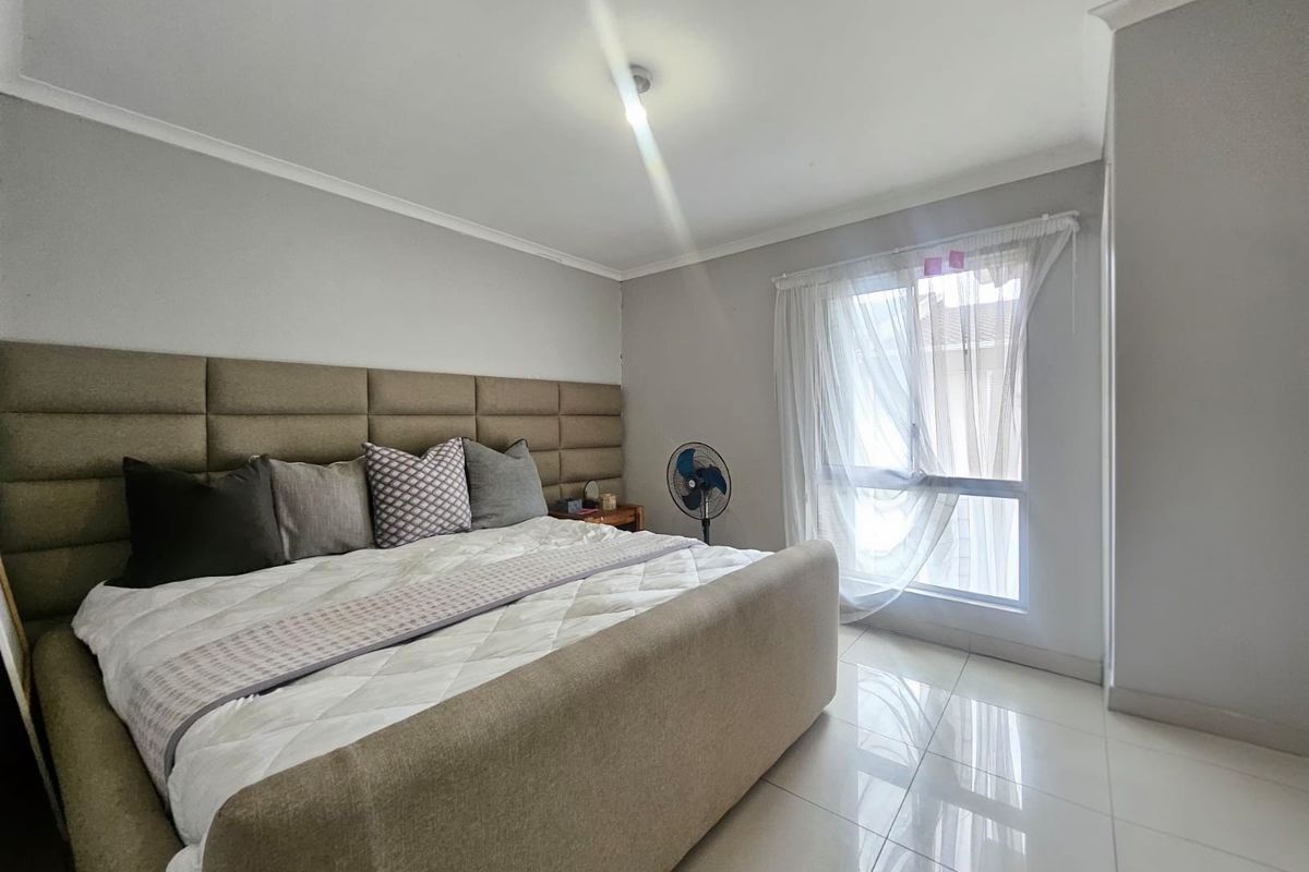 A well-lit bedroom featuring neutral wall tones, tiled flooring, and a large window with sheer curtains.