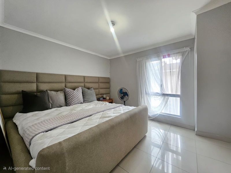 A well-lit bedroom featuring neutral wall tones, tiled flooring, and a large window with sheer curtains.