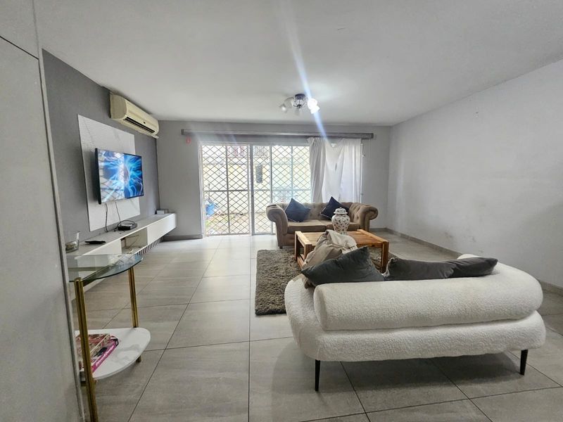 Spacious living room featuring large format floor tiles, a wall-mounted air conditioning unit, and sliding glass doors leading to an outdoor area.