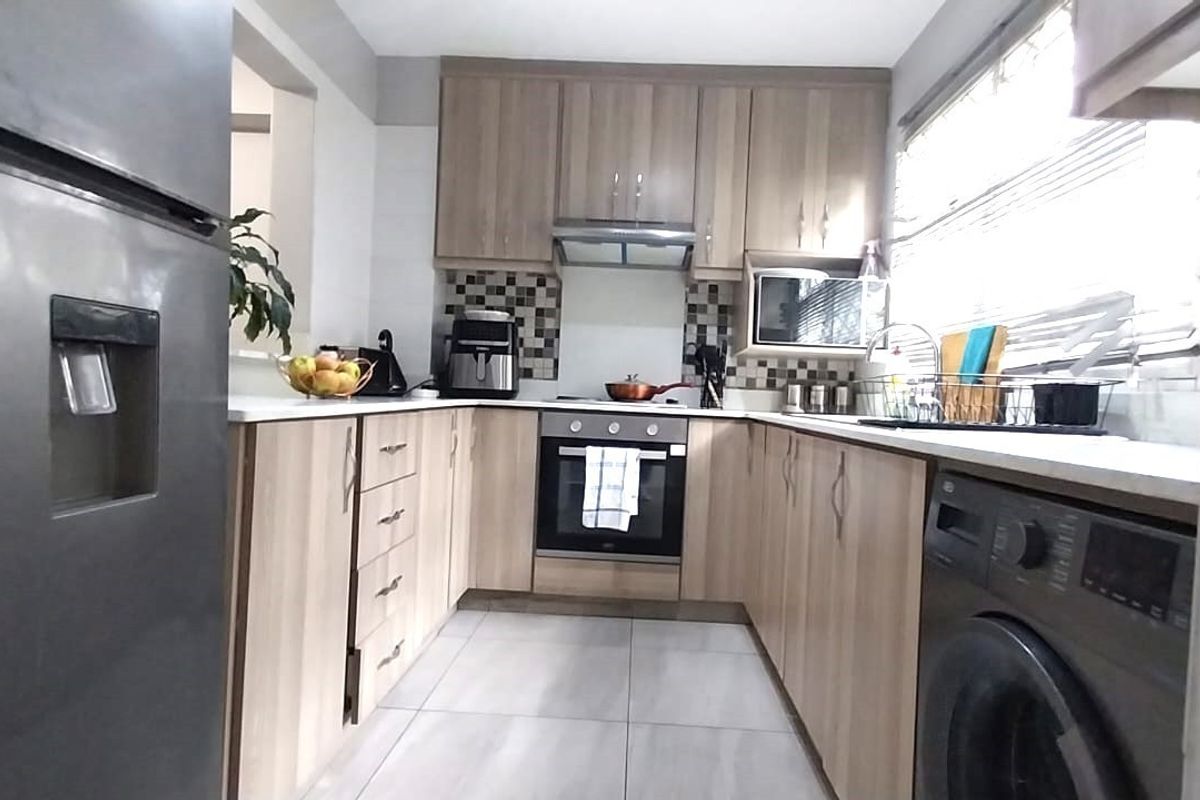 A functional U-shaped kitchen featuring light wood-finish cabinetry, tiled flooring, a built-in oven, and a tiled backsplash.