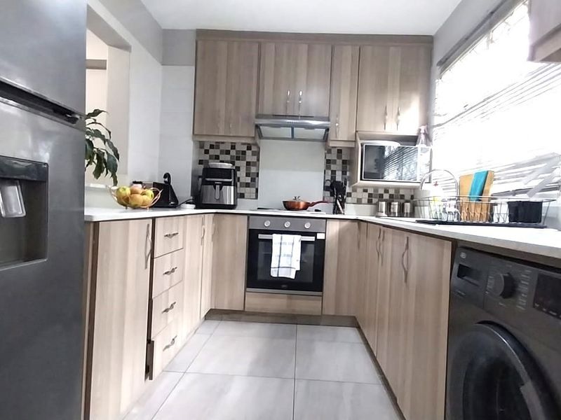 A functional U-shaped kitchen featuring light wood-finish cabinetry, tiled flooring, a built-in oven, and a tiled backsplash.