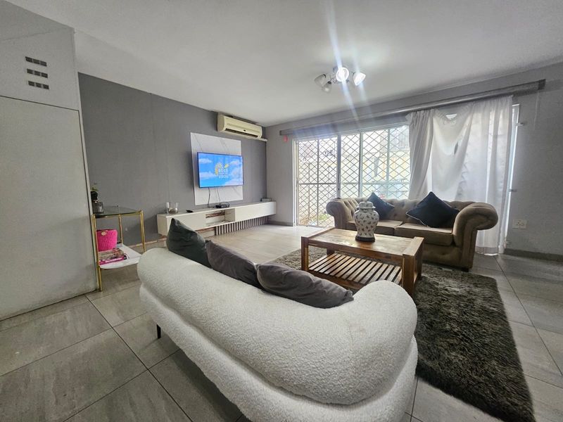 A comfortable living room featuring tiled flooring, a split-system air conditioner, and a sliding glass door with security gate leading to the exterior.