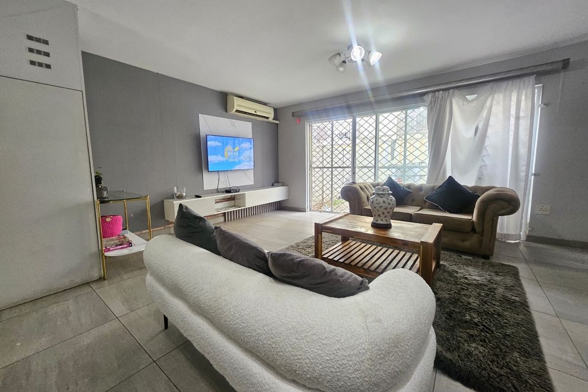 A comfortable living room featuring tiled flooring, a split-system air conditioner, and a sliding glass door with security gate leading to the exterior.