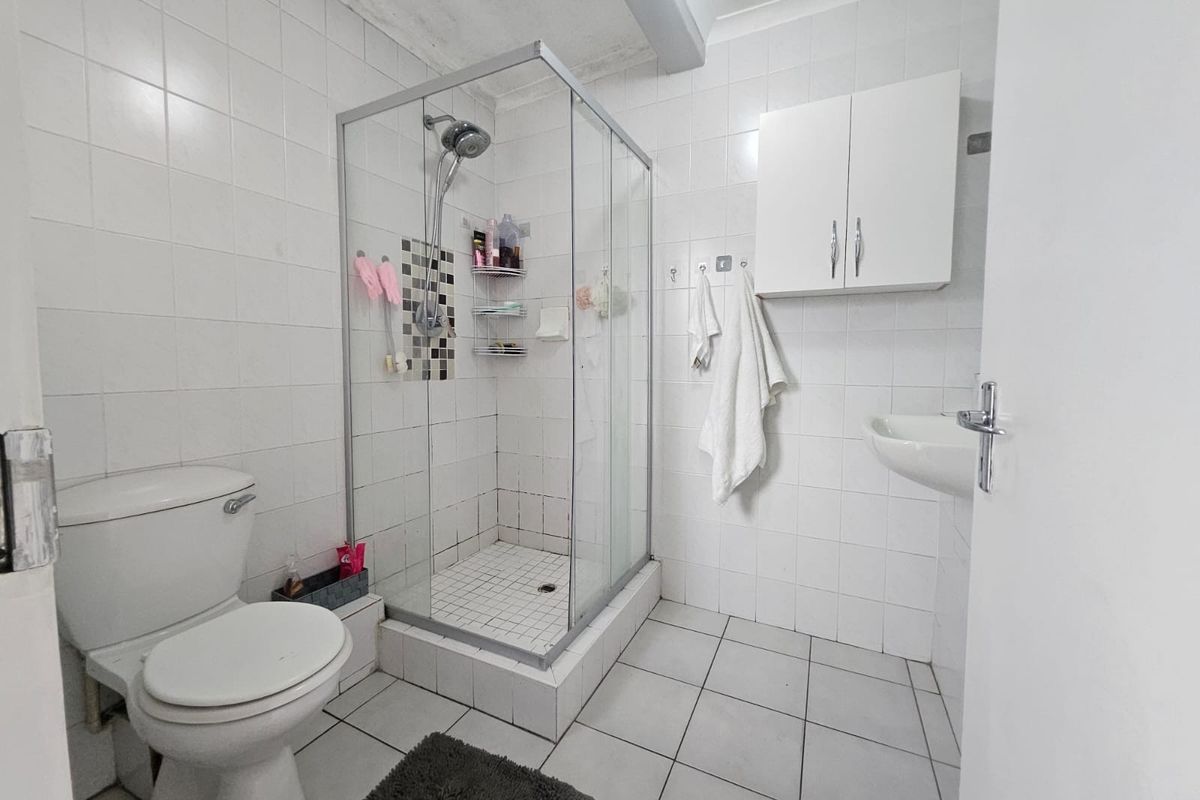 A functional bathroom featuring a glass shower enclosure, wall-mounted basin, toilet, and white wall-mounted storage cabinet with tiled finishes throughout.