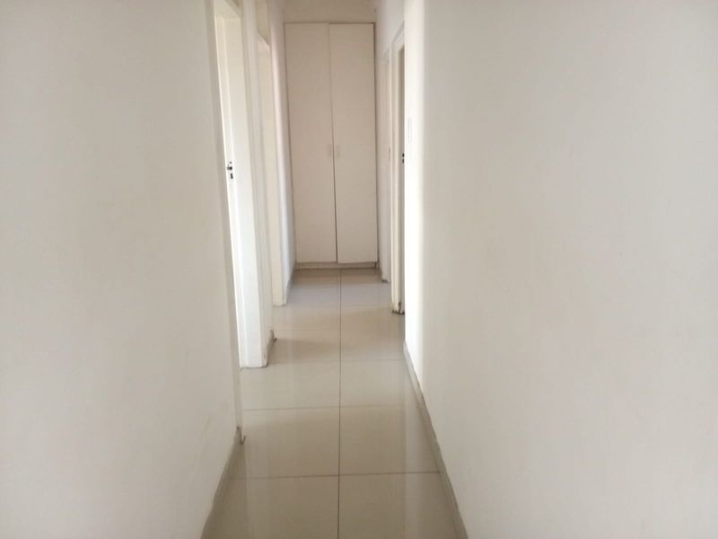 A clean, neutral hallway featuring tiled flooring and a built-in storage cupboard, providing access to various rooms within the apartment.