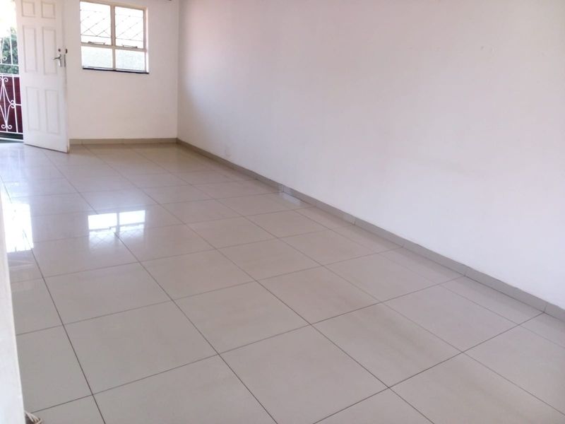 A bright, empty living area featuring neutral ceramic floor tiles, clean white walls, and a security gate leading to an outdoor space.