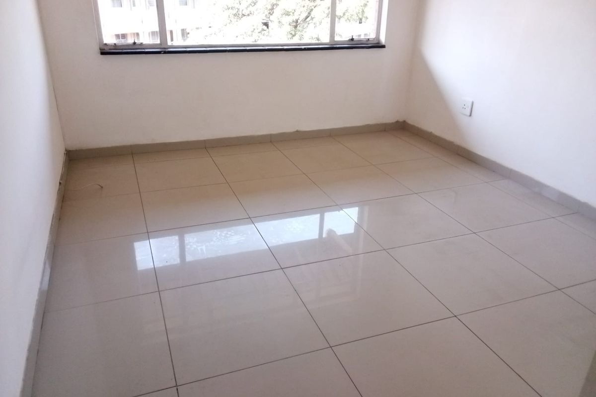 A bright, empty bedroom featuring neutral tiled flooring, clean white walls, and a large window providing natural light.