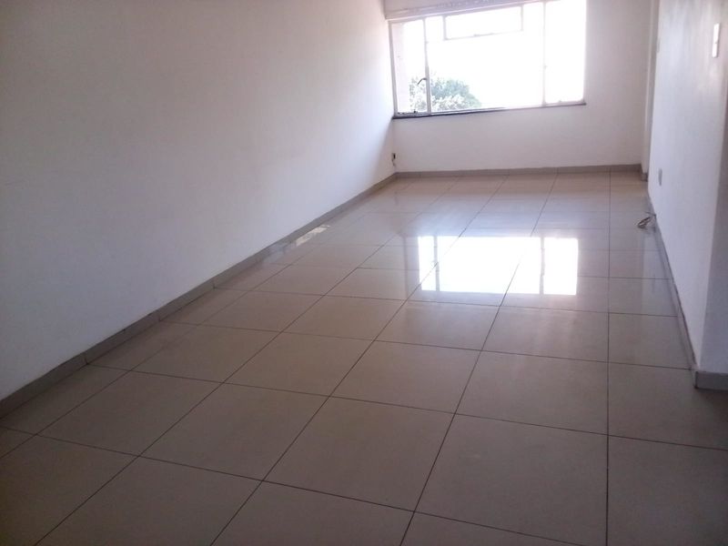 A bright, empty living area featuring neutral tiled flooring and a large window, providing a blank canvas for interior design.