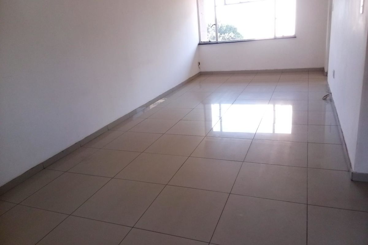 A bright, empty living area featuring neutral tiled flooring and a large window, providing a blank canvas for interior design.
