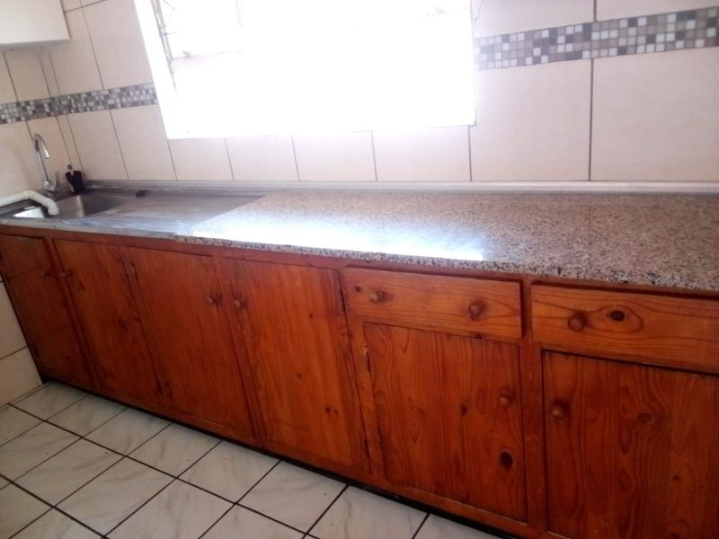 A functional kitchen featuring wooden cabinetry, granite countertops, a stainless steel sink, and tiled backsplash with neutral floor tiles.