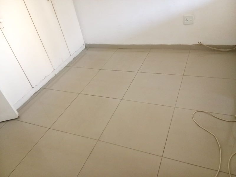 An empty bedroom featuring neutral tiled flooring and built-in cupboards, providing a blank canvas for personalization.
