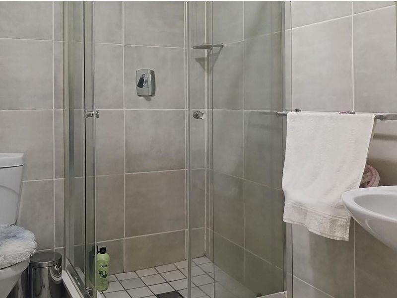 A functional bathroom featuring a glass-enclosed shower, pedestal basin, and neutral wall tiling.