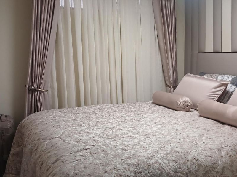 A well-maintained bedroom featuring a neutral color palette, an upholstered headboard, and floor-to-ceiling curtains.