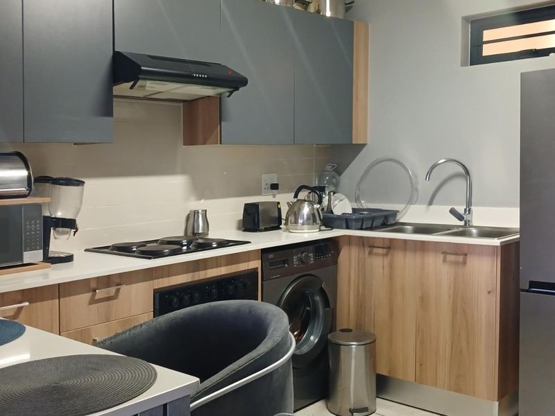 Modern kitchen featuring two-tone cabinetry, laminate countertops, integrated electric hob, oven, extractor fan, and a stainless steel sink with a mixer tap.