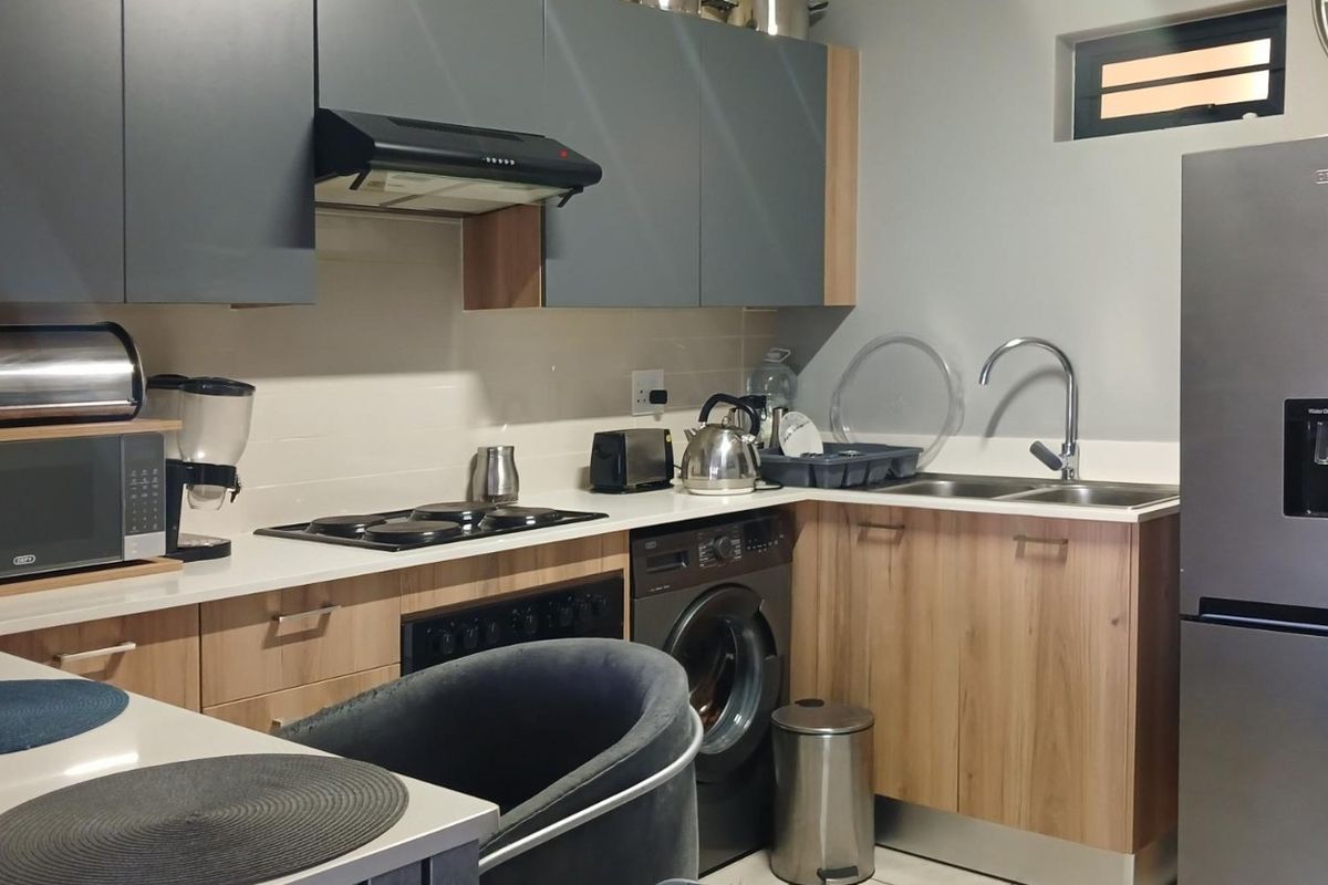 Modern kitchen featuring two-tone cabinetry, laminate countertops, integrated electric hob, oven, extractor fan, and a stainless steel sink with a mixer tap.