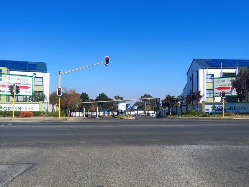 Street view of the Green Park apartment complex entrance, featuring gated security access and solar panel installations on the building roofs.