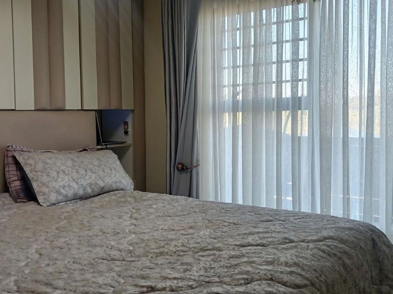 A cozy bedroom featuring a built-in headboard with integrated bedside shelving and large windows dressed with curtains.