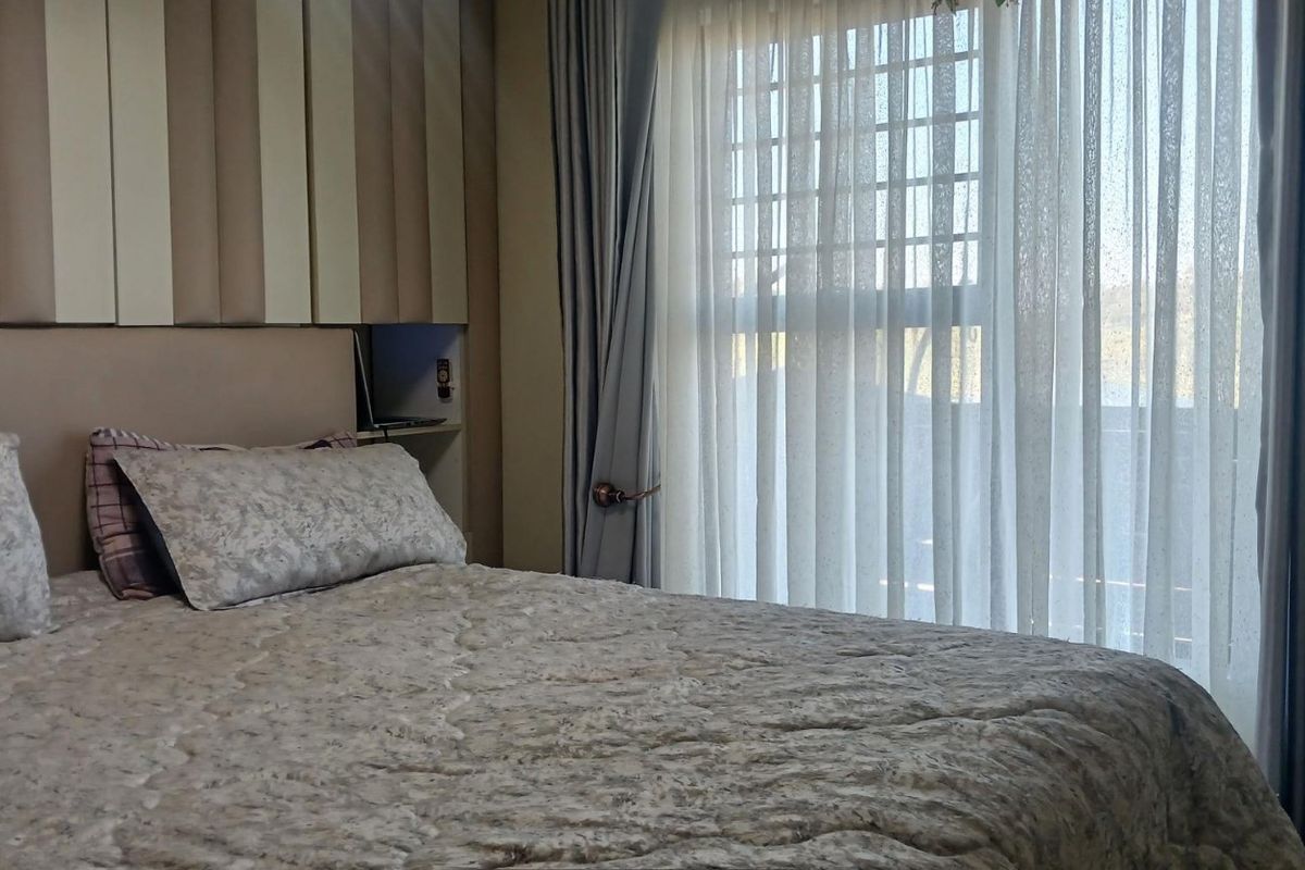 A cozy bedroom featuring a built-in headboard with integrated bedside shelving and large windows dressed with curtains.