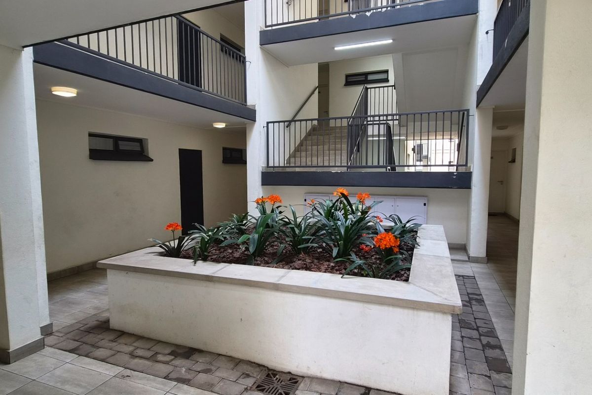 A well-maintained apartment complex courtyard featuring a central raised garden bed, paved flooring, and access to upper-level walkways via a staircase.