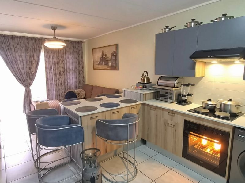 Open-plan living area featuring a modern kitchen with built-in cabinetry, electric hob, oven, and tiled flooring, seamlessly connected to the lounge space.