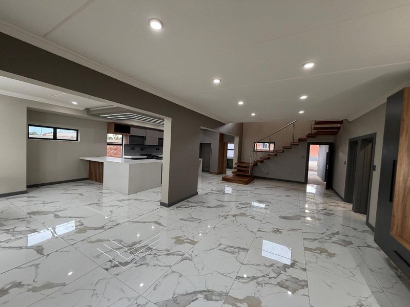 Spacious open-plan living area featuring high-end marble-look floor tiles, a modern floating staircase, and a sleek kitchen with a central island.