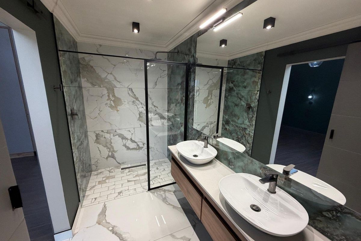 Modern bathroom featuring a spacious walk-in shower with glass screen, double vanity with vessel sinks, and elegant marble-effect tiling throughout.