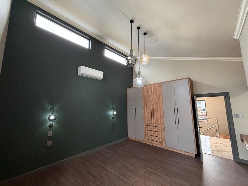 A modern, spacious bedroom featuring built-in cupboards, sleek laminate flooring, split-system air conditioning, and stylish pendant lighting with high-set windows.