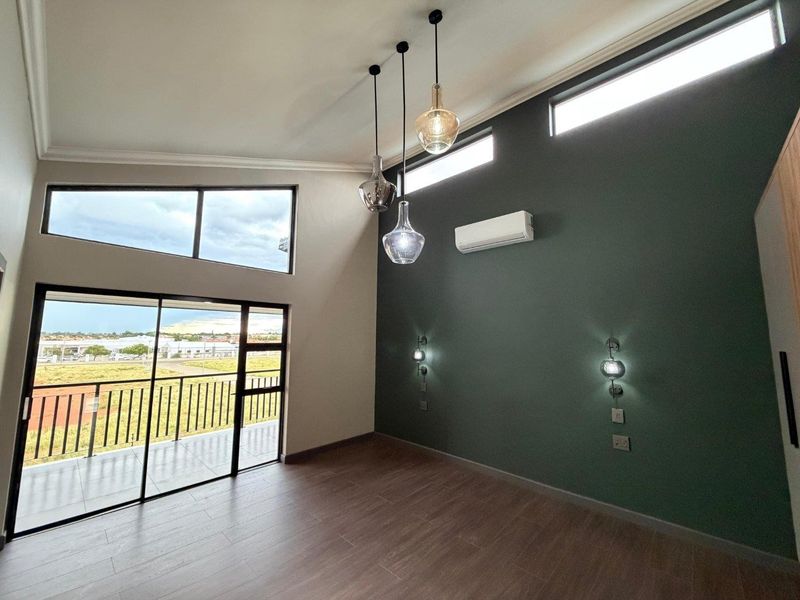 Spacious bedroom featuring high vaulted ceilings, clerestory windows, modern pendant lighting, and a private balcony with expansive views.