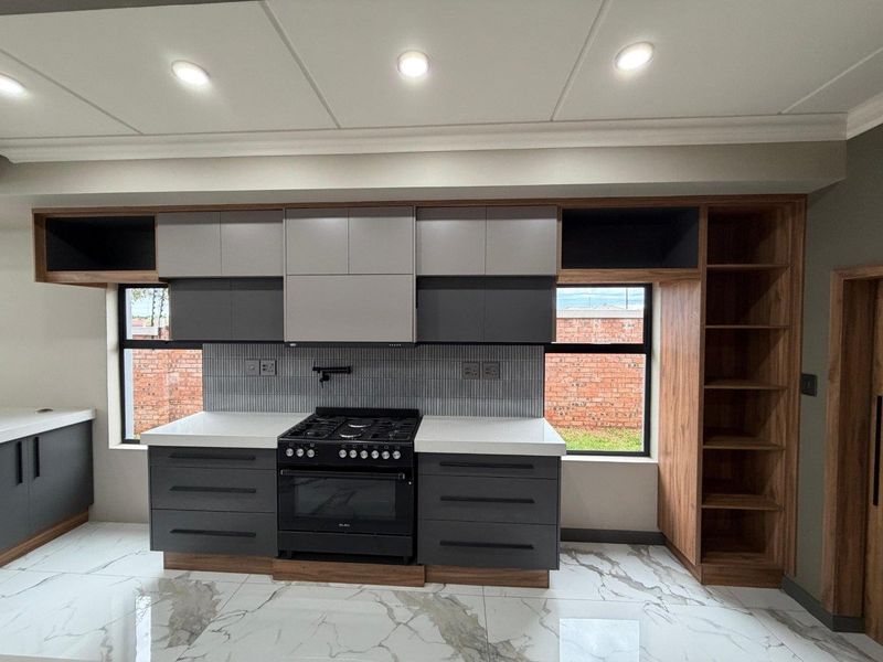 Modern kitchen featuring sleek two-tone cabinetry, stone countertops, a gas stove with extractor, and elegant marble-look floor tiles.