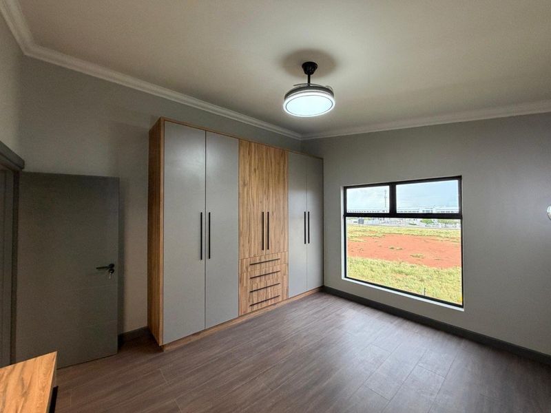 A modern, empty bedroom featuring sleek built-in cupboards with wood and grey finishes, laminate flooring, and a contemporary ceiling fan.