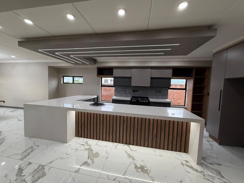 Modern, newly renovated kitchen featuring a large island with stone countertops, integrated cabinetry, gas hob, and stylish recessed ceiling lighting with marble-look flooring.