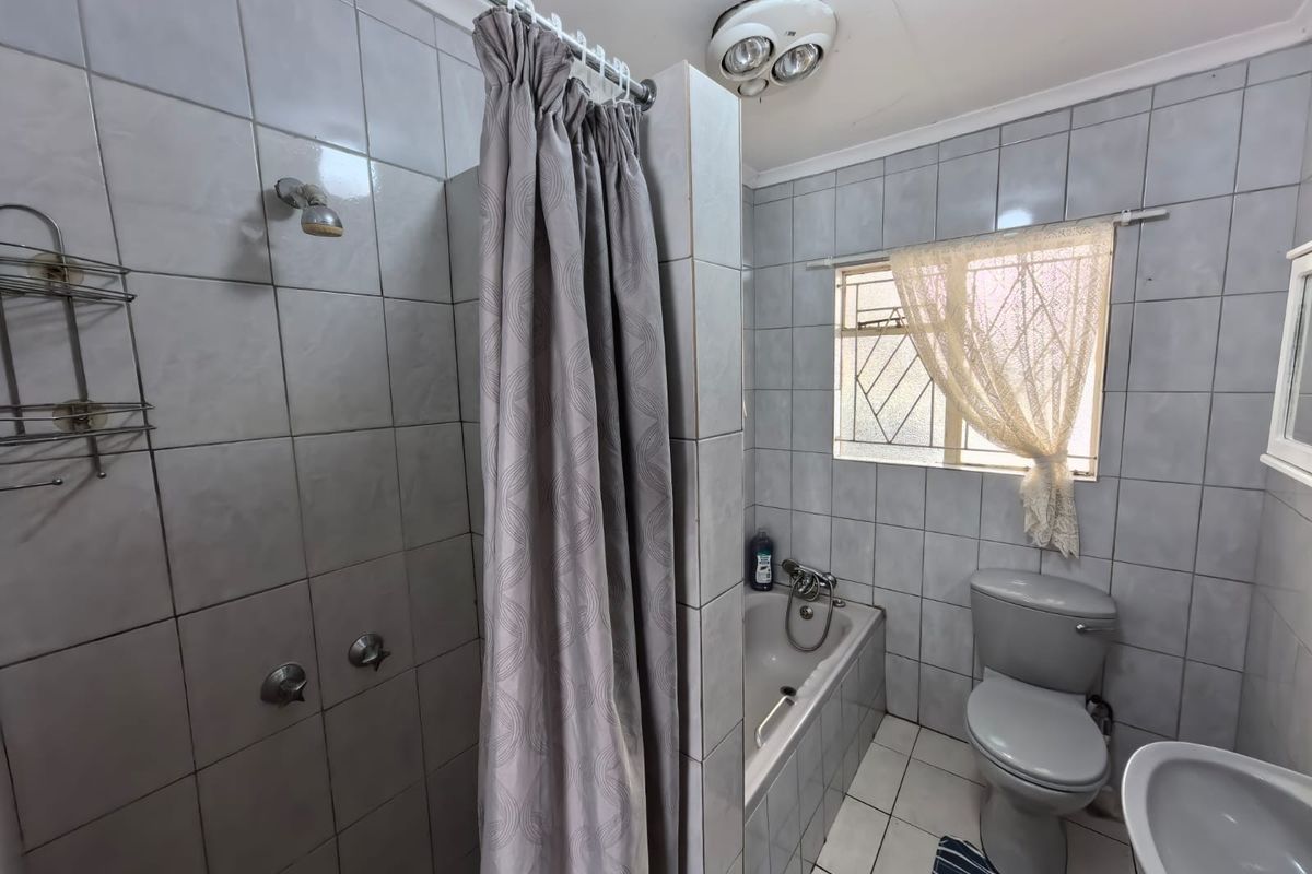 A functional bathroom featuring a combined shower and bathtub, toilet, and washbasin with tiled finishes and a ceiling heater.