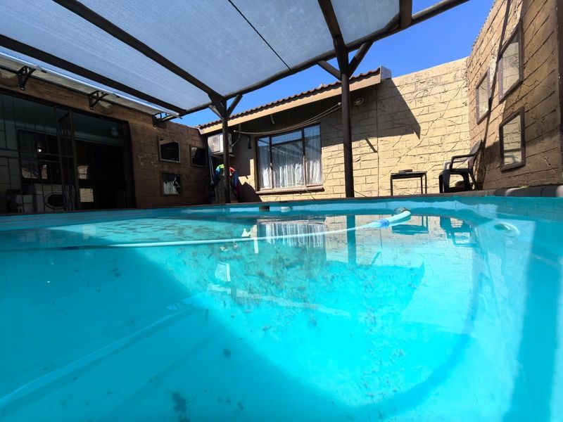 Outdoor pool area featuring a swimming pool covered by a shade sail structure, set against a stone-clad boundary wall.