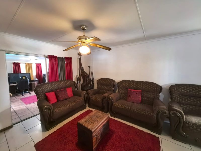 A living room featuring tiled flooring and a ceiling fan, with an open transition to an adjacent room.