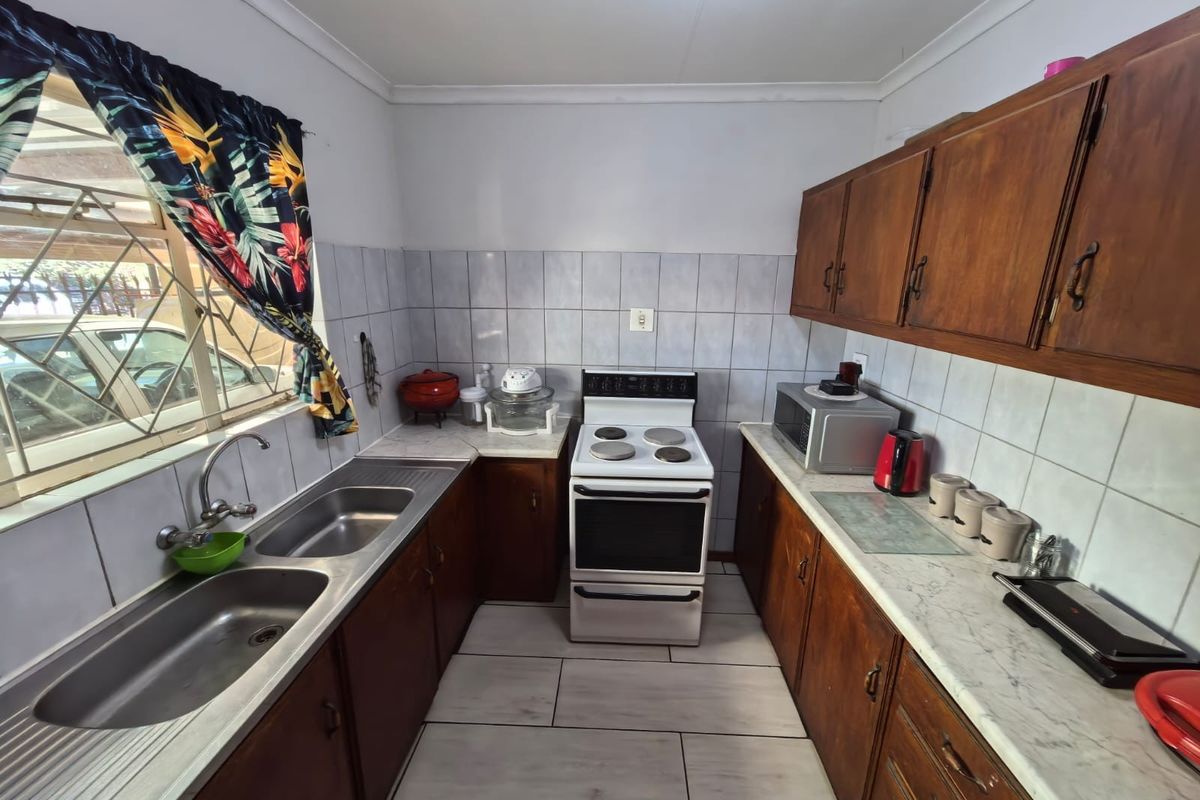 A functional kitchen featuring wooden cabinetry, a double stainless steel sink, tiled splashbacks, and a freestanding electric stove.