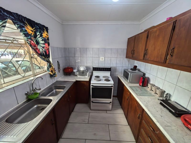 A functional kitchen featuring wooden cabinetry, a double stainless steel sink, tiled splashbacks, and a freestanding electric stove.