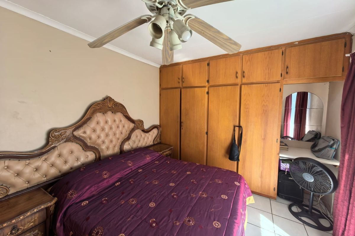 A bedroom featuring built-in wooden cupboards, a vanity area, tiled flooring, and a ceiling fan.