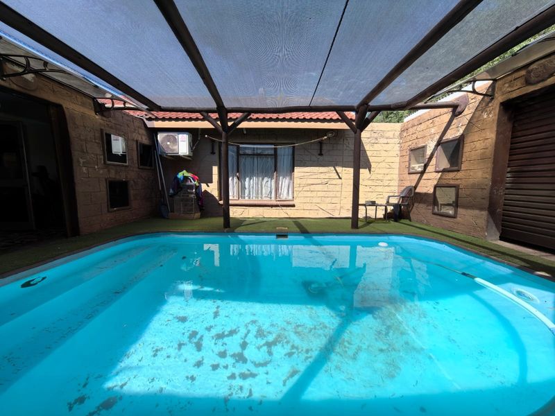 Outdoor pool area featuring a swimming pool, shade sail structure, and textured stone wall cladding, requiring maintenance and cleaning.