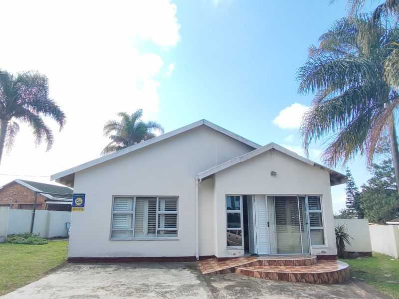 Front elevation of a single-story house featuring a concrete driveway, tiled entrance steps, and aluminium-framed windows set within a fenced garden.