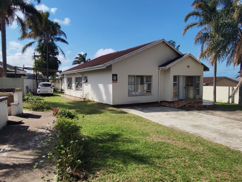 Front view of a single-story house featuring a concrete driveway, lawn, and a built-in brick braai area in the side yard.