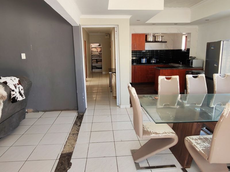 Open plan living and dining area featuring tiled floors, recessed lighting, and a connected kitchen with dark cabinetry and a black tiled backsplash.