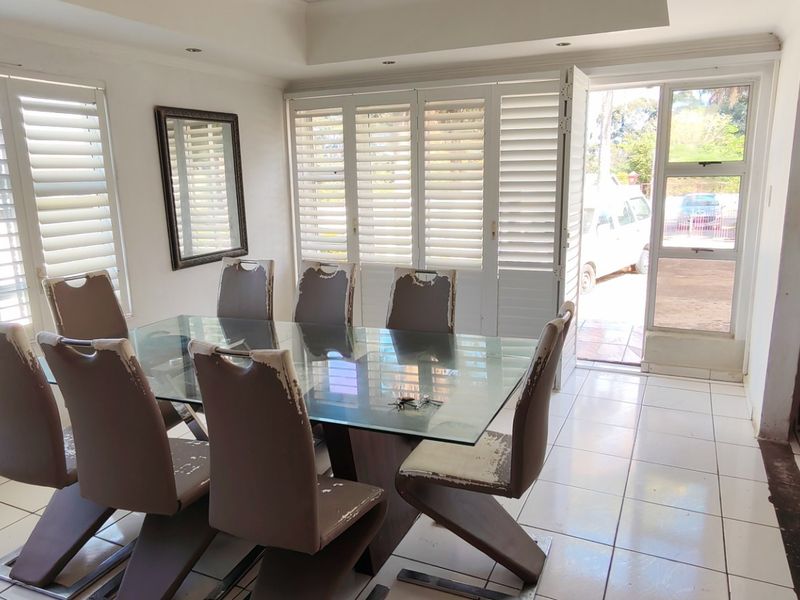 A bright dining room featuring white plantation shutters, tiled flooring, and direct access to the exterior through a glass door.