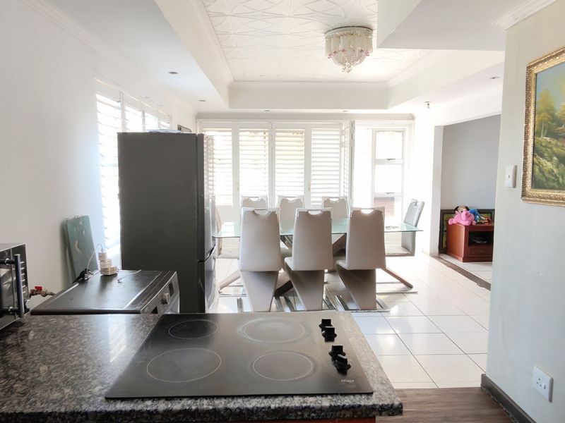 Open-plan kitchen and dining area featuring granite countertops, an electric hob, tiled flooring, and a decorative coffered ceiling with plantation shutters.