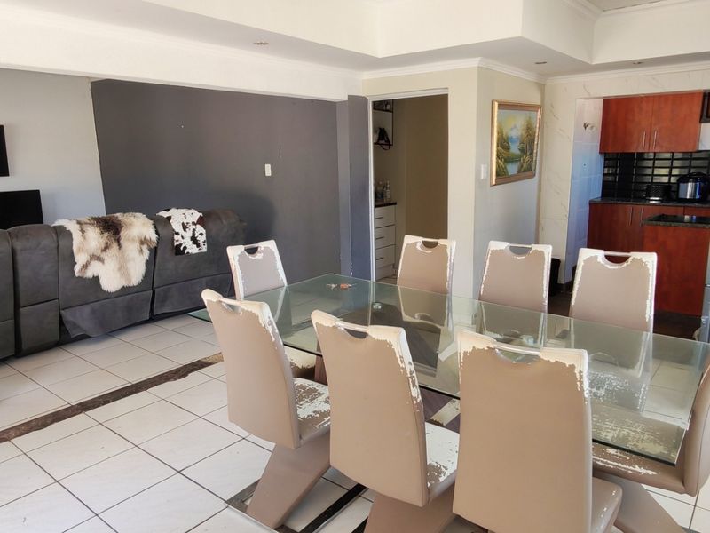 Open-plan living and dining area featuring tiled flooring, recessed lighting, and an adjacent kitchen with dark cabinetry and a tiled backsplash.