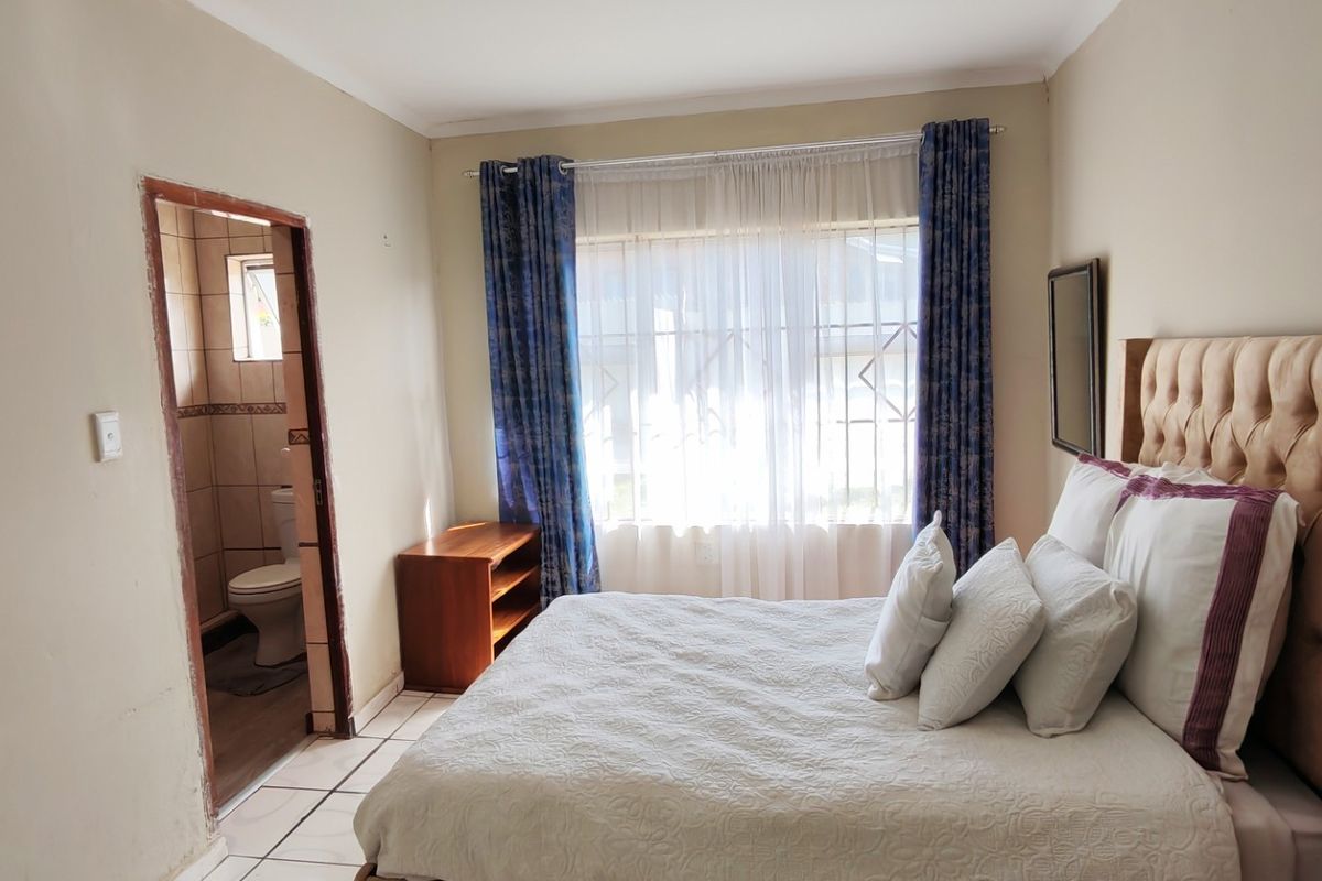 A bedroom featuring tiled flooring, a window with security bars, and direct access to an en-suite bathroom.