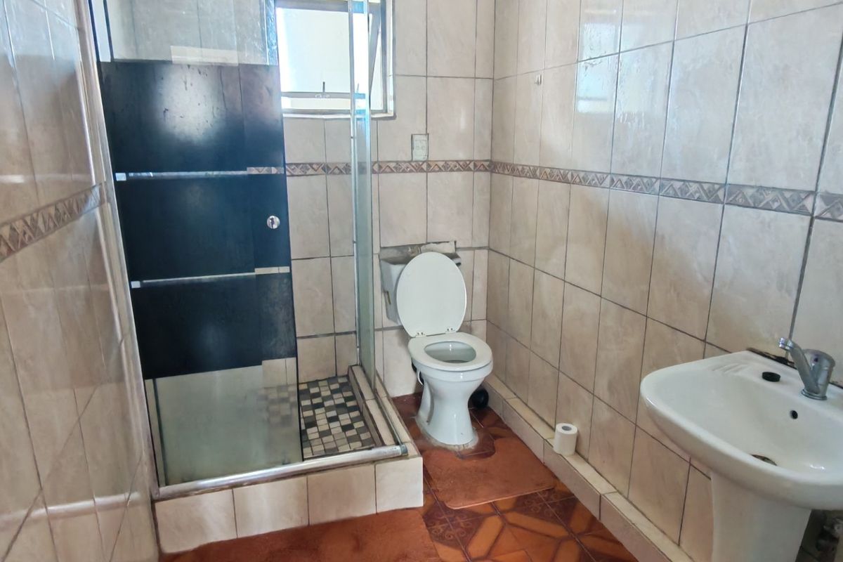 A functional bathroom featuring a shower enclosure, pedestal basin, and toilet, finished with full-height wall tiling and floor tiles.
