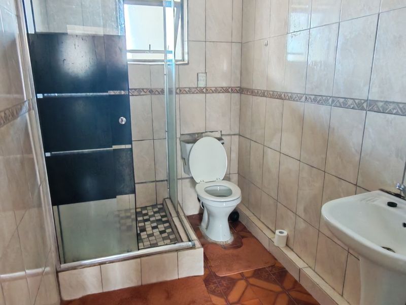 A functional bathroom featuring a shower enclosure, pedestal basin, and toilet, finished with full-height wall tiling and floor tiles.