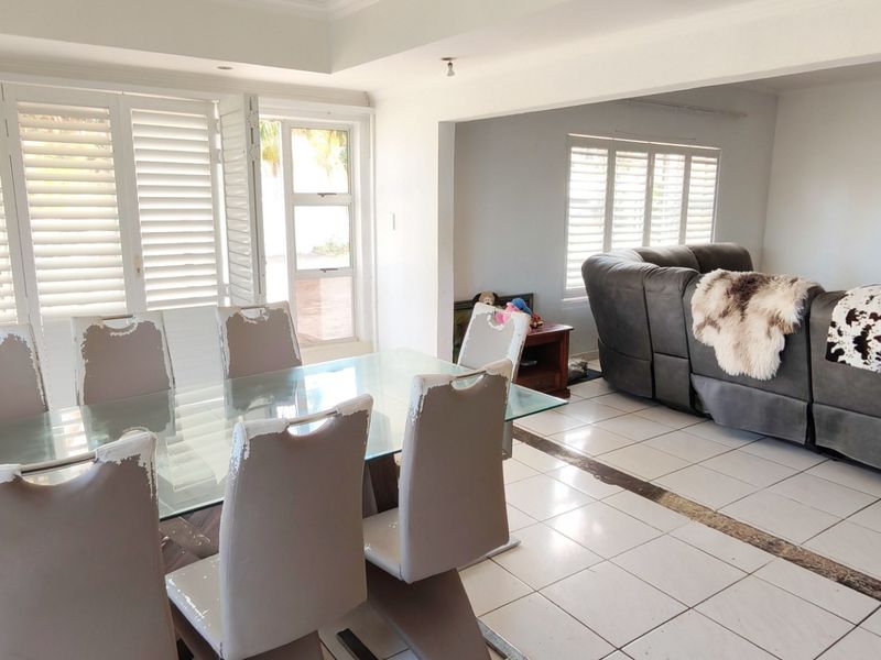 Spacious open-plan living and dining area featuring white ceramic floor tiles, recessed lighting, and plantation shutters providing ample natural light.